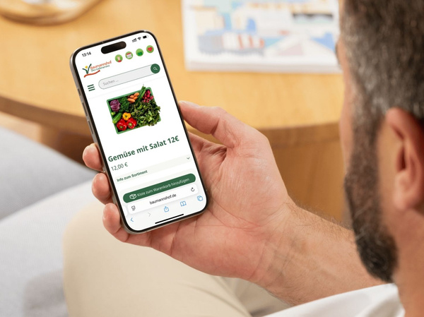 Ein Mann hält ein Smartphone mit der Baumannshof-Webseite in der Hand.