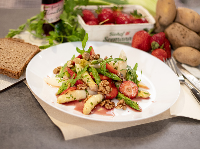 KI generiert: Salat mit Spargel, Erdbeeren und Walnüssen auf einem Teller, daneben Erdbeerkorb, Kartoffeln und Brot. Text: "Biohof Sensler".