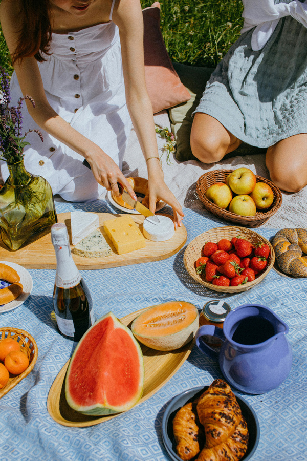 KI generiert: Picknick mit Früchten, Käse, Croissants und Sekt auf einer Decke im Freien.