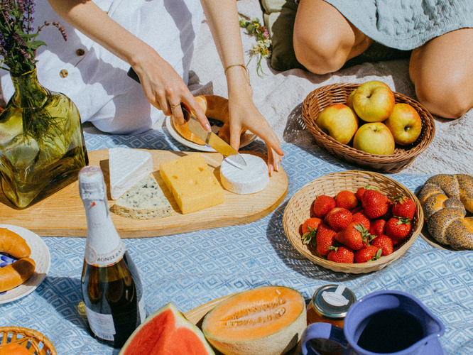 KI generiert: Ein Picknick mit Käse, Früchten und Getränken auf einer Decke im Freien.