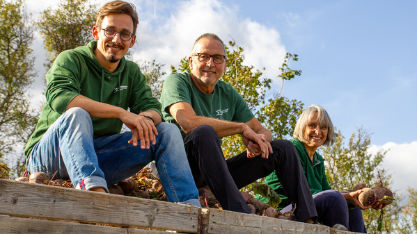 KI generiert: Drei Personen sitzen lächelnd auf einer Holzbank in der Natur.