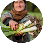 Frau steht auf einem Acker, hält Lauch in die Kamera.