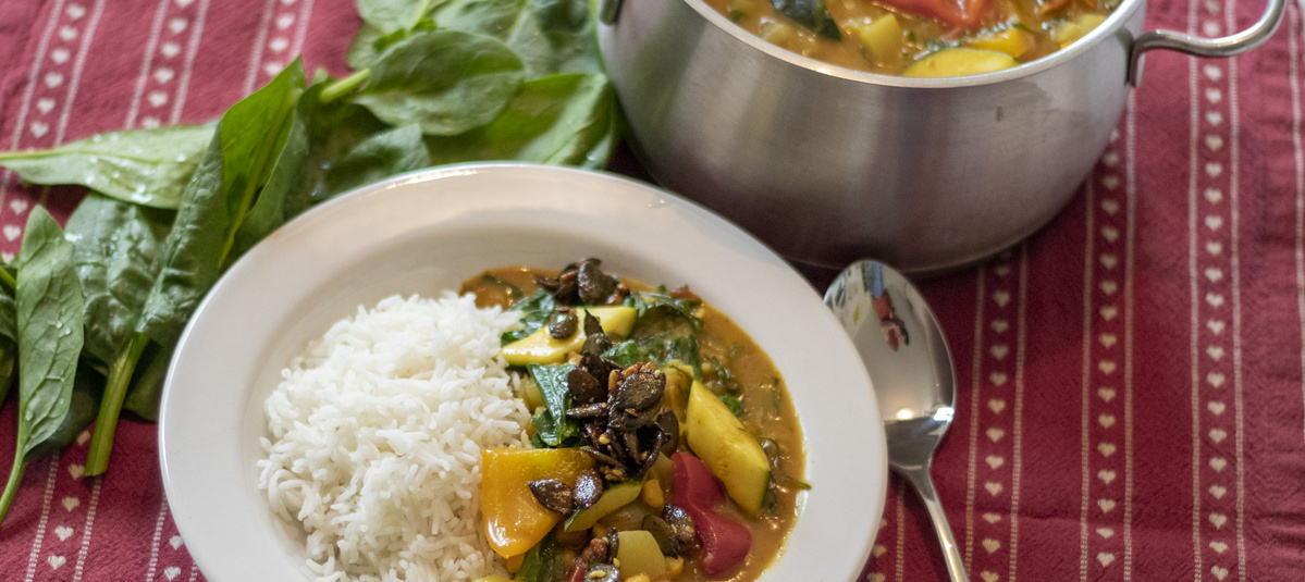 Gemüsecurry mit Reis im Teller und frischen Spinat außen liegend