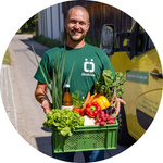 Mitarbeiter des Baumannshofs steht mit einer Ökokiste neben dem gelben Lieferauto.