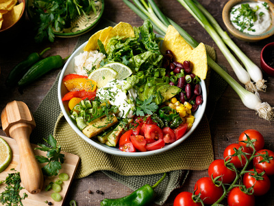 Bunte Gemüseschale mit Bohnen, Tomaten, Salat und Tortillachips, garniert mit Limette und Kräutern.