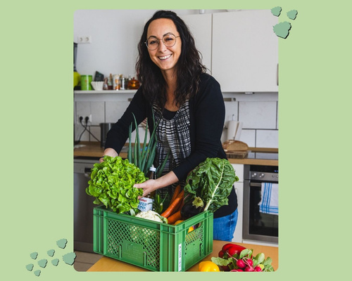 Frau lacht und packt Ökokiste mit frischem Gemüse aus